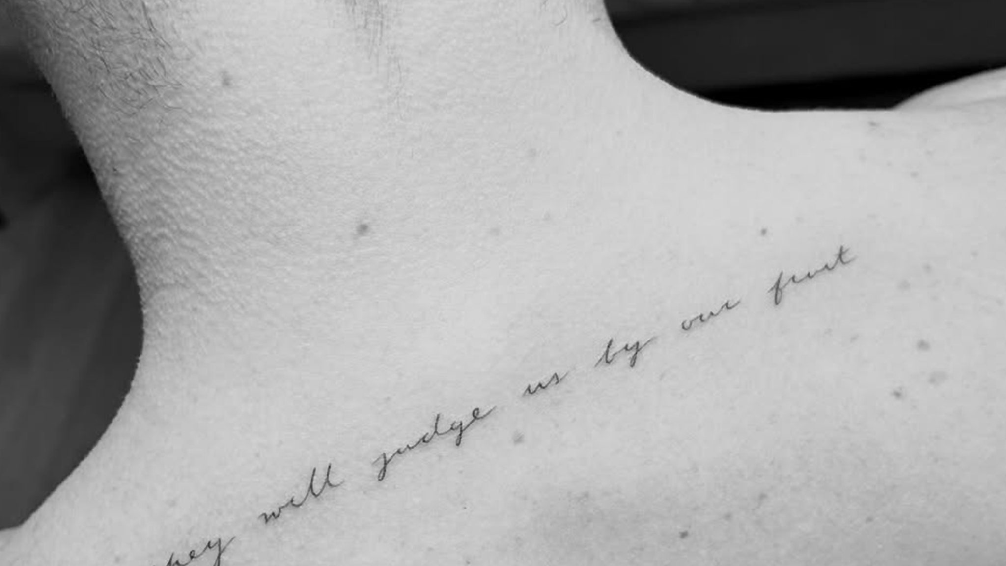Source photo showing Chase Stokes’s fine-line cursive tattoo across his upper back.