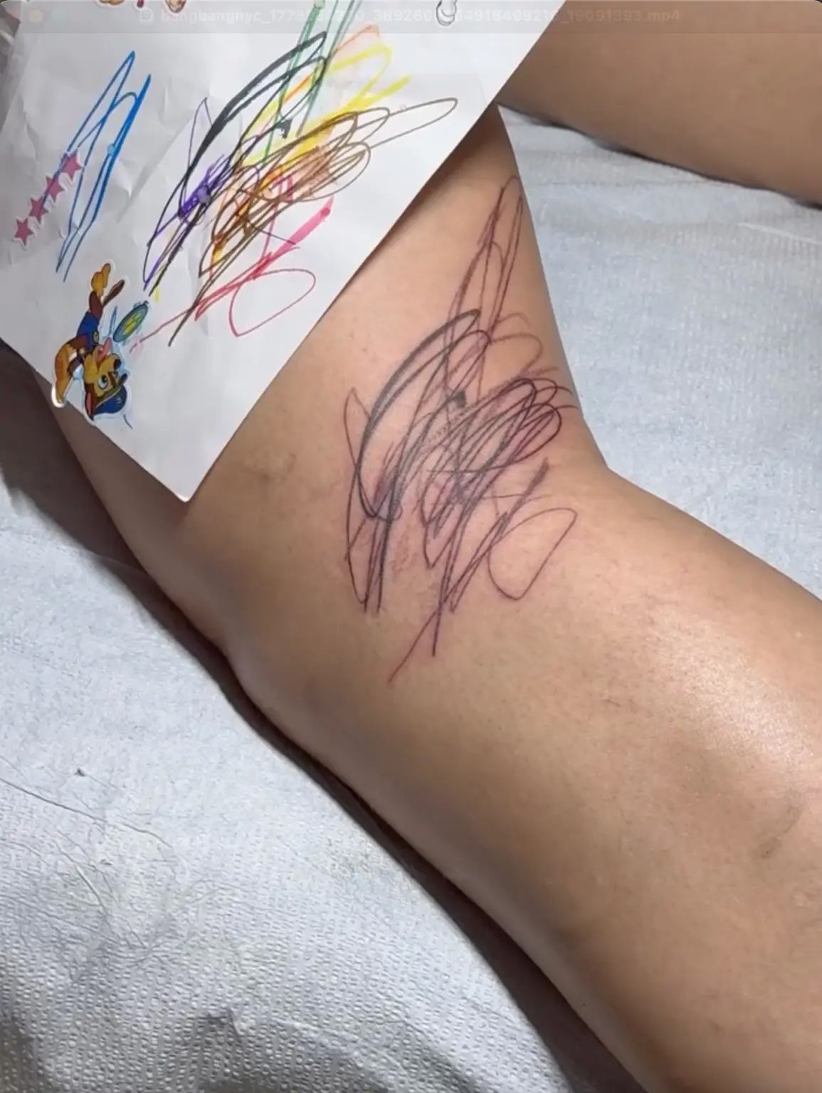 Source photo showing black scribble tattoo linework at the back of Rihanna’s knee beside the original children’s drawing